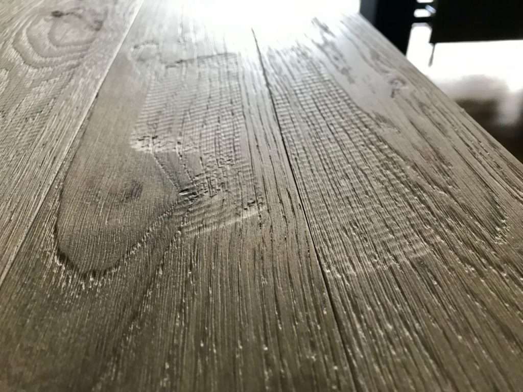 factory worker manually scraping engineered oak plank with traditional hand tool